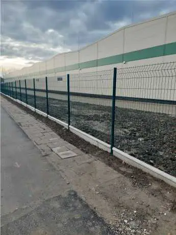 Zöld táblás kerítés ipari épület mellett